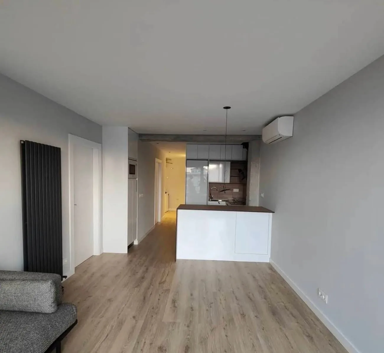 Salón con cocina abierta, península blanca y radiador vertical