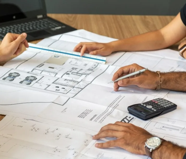 Manos revisando planos de una reforma con regla y calculadora