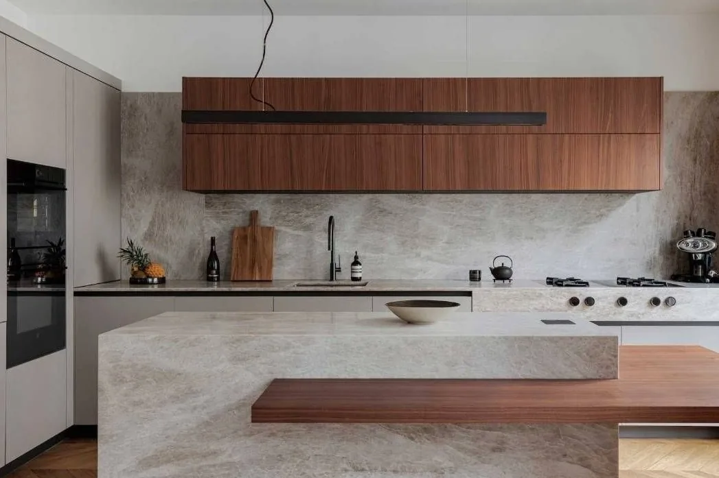 Cocina con isla de efecto mármol, barra de madera y muebles altos de madera